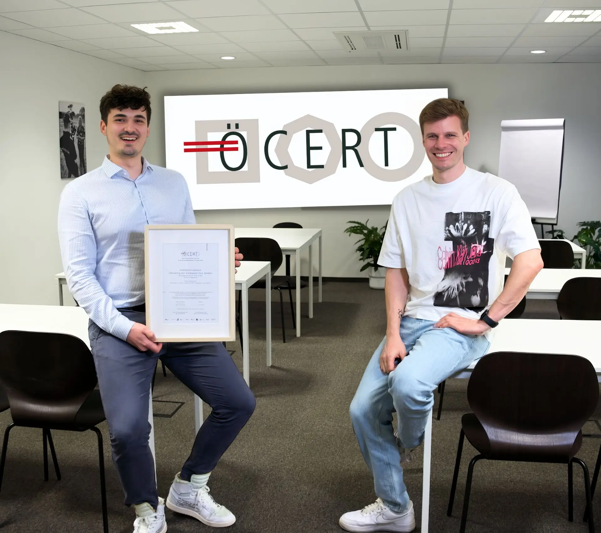 Zwei Kursteilnehmer mit ÖCERT-Zertifikat im mediapool campus Seminarraum; großes ÖCERT-Logo im Hintergrund